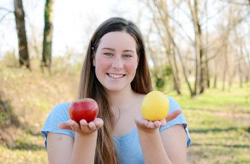 Young happy woman is standing in park and eating apple.