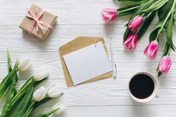 Cup of coffee with gift, tulips and blank sheet of paper on wooden background for Mother's Day.