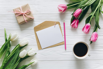 Cup of coffee with gift, tulips and blank sheet of paper on wooden background for Mother's Day.