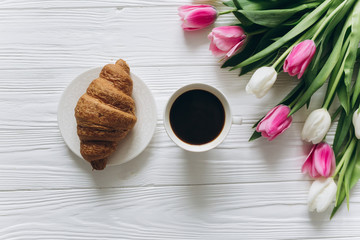 Cup of coffee with croissant and fresh tulips on wooden background for Mother's Day.