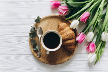 Fototapeta premium Cup of coffee with croissant and fresh tulips on wooden background for Mother's Day.