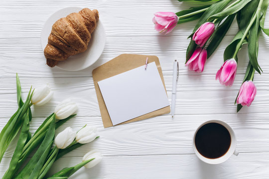 Cup of coffee with gift, tulips and blank sheet of paper on wooden background for Mother's Day.
