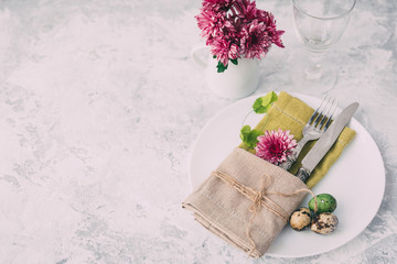 Easter table place setting with blank plate, flowers decoration, cutlery and decor egg on light background, top view. Spring or Easter food concept. Green tones
