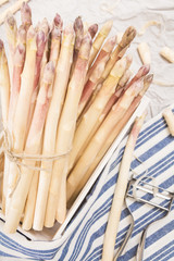 Bunch of white asparagus in box, on crumpled paper with metallic peeler and kitchen towel.