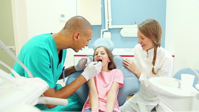 Friendly woman dentist talks with young patient while male surgeon examines her