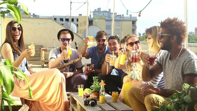 Group of happy multi-ethnic friends looking at camera and toasting with cocktails at rooftop party on beautiful sunny day, graded