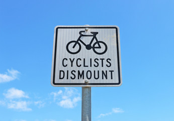 black and white Cyclists Dismount sign in a blue sky
