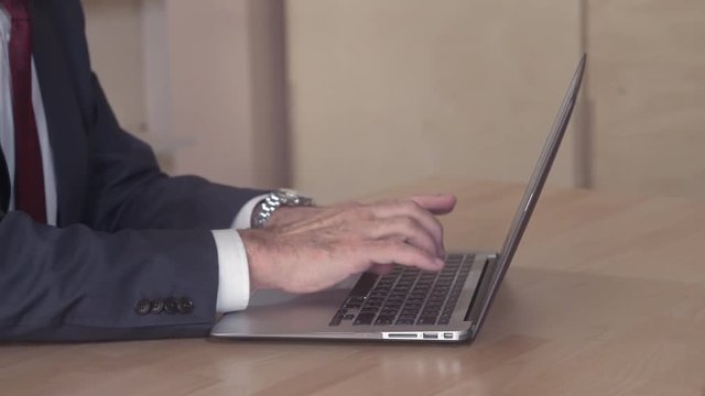 Closeup detail man entering data on computer. Male hands typing on keyboard laptop and the close it. Businessman wearing formal suit and red tie.