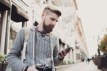 Outdoor portrait of modern young traveler man using smart phone on the street