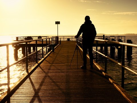 Alone tourist takes photos with camera and tripod on wooden pier