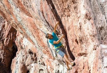 Male Rock Climber on high orange natural stone Wall