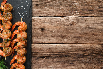 Japanese seafood. Fried spicy shrimps with herbs on wooden skewers served on black slate, flat lay. Rustic wooden background with free space for text. Menu photo.