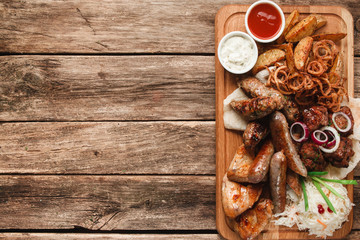 Mix of delicious tasty grilled meat free space. Snacks for beer served with pita bread, fried potato wedges,onion rings and sauerkraut on rustic wooden table. Restaurant menu photo.