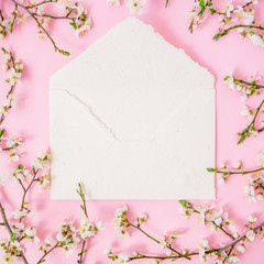 Round frame of spring white flowers and white paper envelope on pink background. Flat lay, top view. Spring time background.