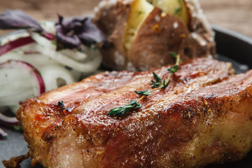 Juicy grilled beef steak decorated with herbs, served with baked potato and onion rings, close up view. American cuisine. Menu photo.
