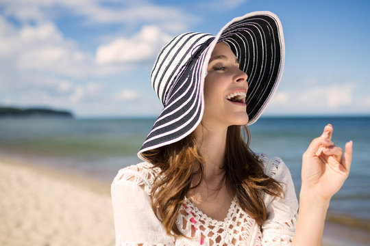 Beautiful woman in hat standing on beach laughing