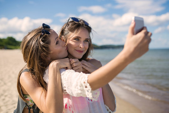 Two beautiful female friends taking selfie on beach having fun