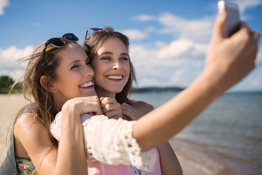 Two beautiful female friends taking selfie on beach