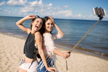 Two happy women taking selfie on beach fooling around