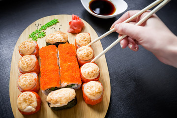 Sushi rolls, sauce and woman hand on a black background. Japanese food. Top view. Flat lay