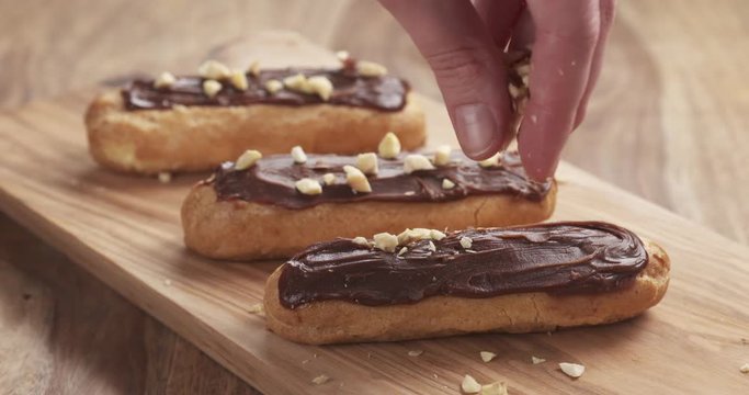 Slow motion of decorating eclairs with hazelnuts on wood board, 4k 60fps prores footage