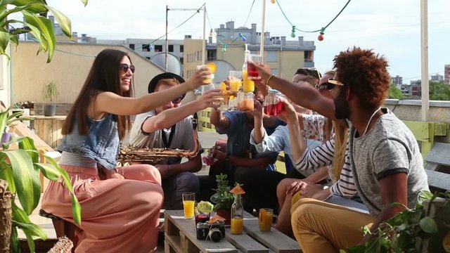 Cheerful multi-ethnic friends looking at camera, laughing and toasting with cocktails at rooftop party on beautiful sunny day