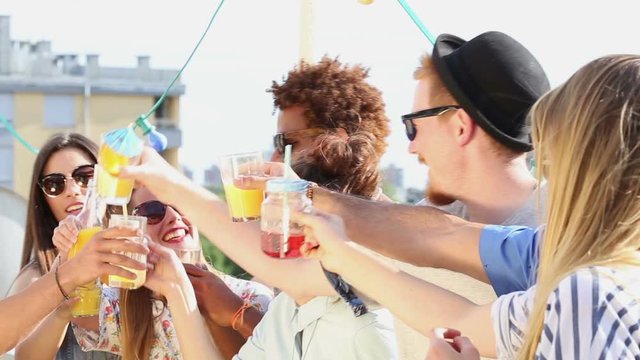 Side view of happy young multi-ethnic friends laughing and toasting at rooftop party 