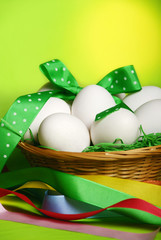 Basket of Easter white eggs with joyful colorful ribbon over green yellow background and copy space 