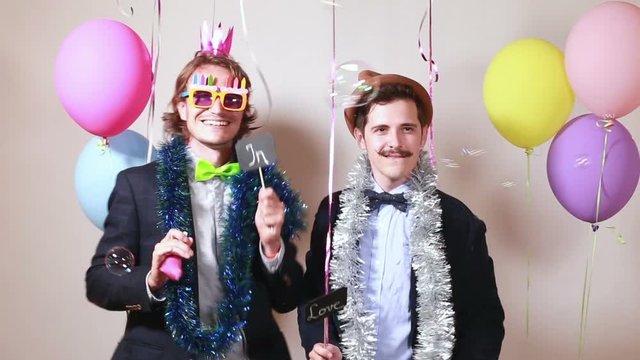 Two funny men holding boards in love in party photo booth 