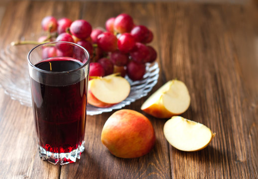 Grape juice in a glass beaker, grapes and apples on a wooden background. Fruit mix