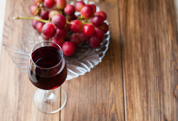 Grape wine in a glass cup, a bunch of grapes on a wooden background.
