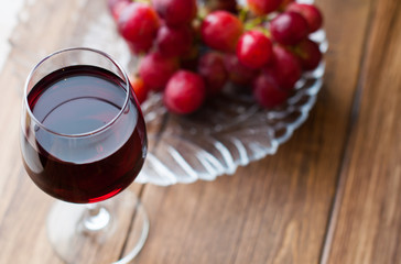 Grape wine in a glass cup, a bunch of grapes on a wooden background.