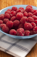 a blue bowl filled with red raspberries over vintage rustic dishtowel on wood table 