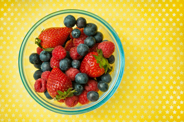 various fruit - raspberries and blueberries - in a bowl over yellow background 