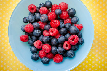 various fruit - raspberries and blueberries - in a bowl over yellow background 