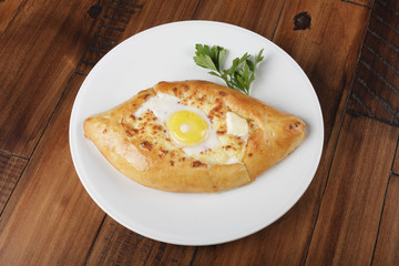 Khachapuri - traditional georgian pie with egg, potatoes and cheese. Cake on a white plate. Wooden background