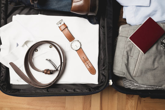 Open traveler's bag with men clothing, accessories, watch, leather shoes, passport and belt. Travel and vacations concept. 