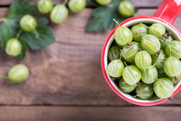Fresh berries gooseberries close-up in a mug on a wooden table. © Dimorozov