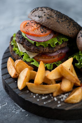 Closeup of black burger on sesame bun served with potato wedges, selective focus