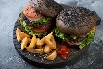 Wooden serving board with a pair of black beef burgers, fried potato and ketchup