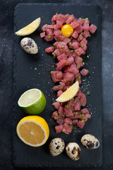 Fototapeta na wymiar Top view of tuna tartar served with quail egg yolk, lemon and lime on a stone slate tray