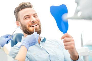 Handsome male patient looking at his beautiful smile sitting at the dental office