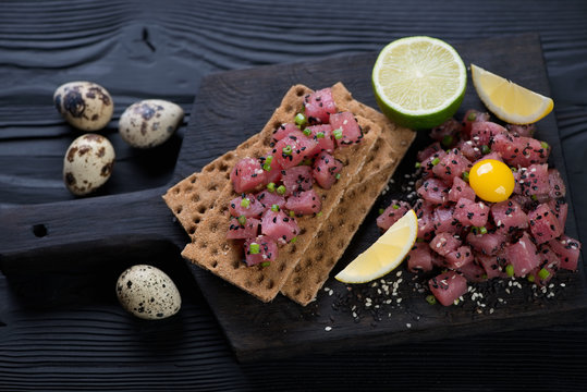 Black wooden serving board with fresh tuna tartare, selective focus, studio shot