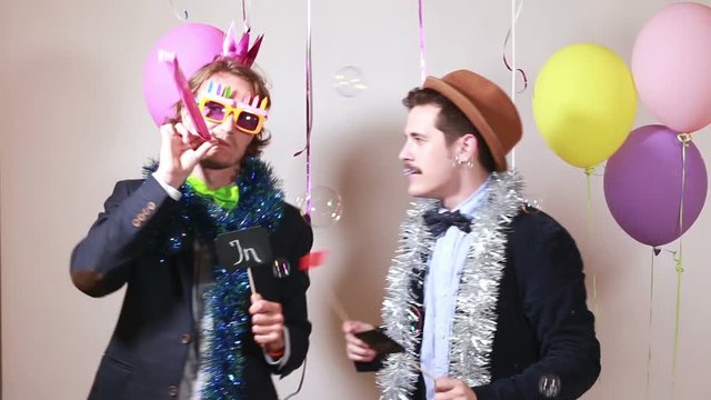 Two funny male friends having fun with props in photo booth