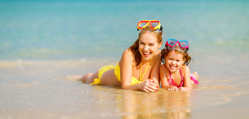 Happy family mother and chid daughter in masks on beach in summer