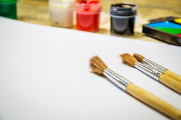 Paint brushes and a white sheet of paper. Composition of watercolor and gouache paints on a wooden background.
