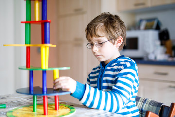Kid boy with glasses playing with lots of colorful wooden blocks game indoor