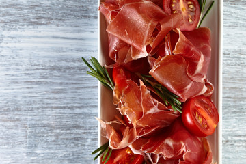  Prosciutto with  rosemary and tomato on a wooden table, free space for your text