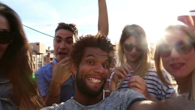 Close up of happy crazy multi-ethnic group of friends filming themselves at rooftop party on sunny day