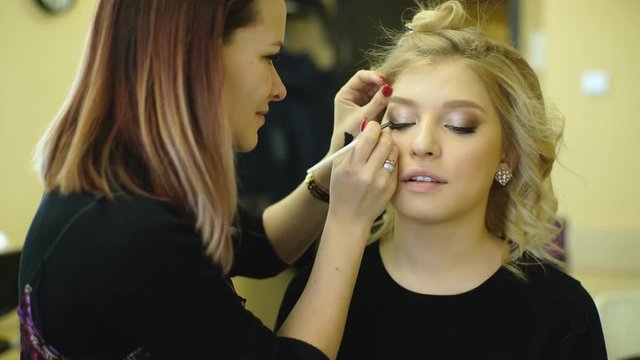 Young beautiful woman applying make-up by make-up artist